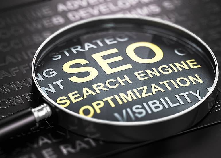 magnifying glass on a piece of text highlighting the words SEO search engine optimisation. Adobe stock.