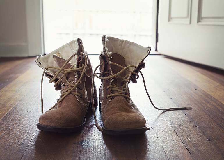 a pair of mens worn out tradie boots in a hallway of a home.