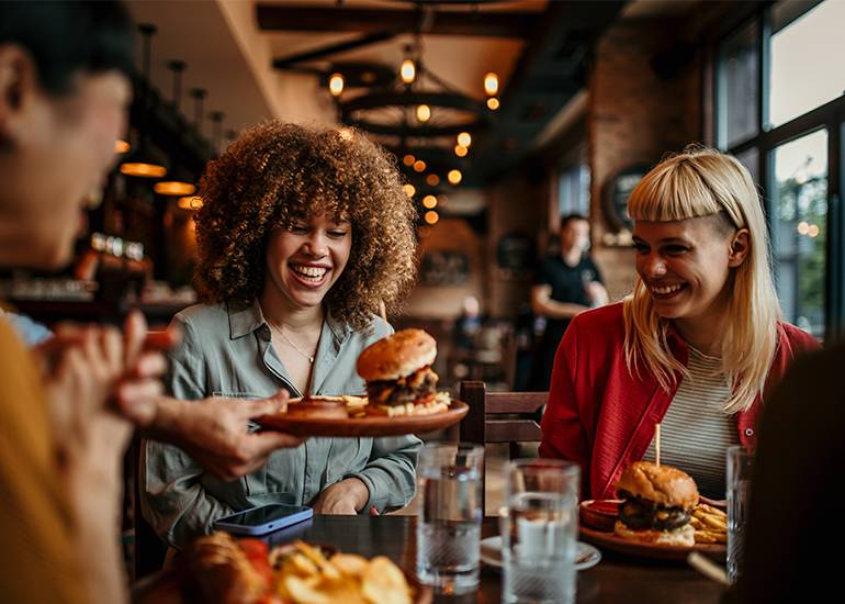 Waiter serving a burger to a trio of women at a restaurnt